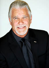 headshot portrait of Bazzel Baz with grey hair and goatee, dressed in black shirt and black sportcoat, smiling