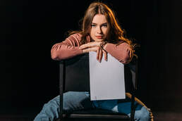 young female writer sitting on chair backwards looking into camera resting her chin on her hands